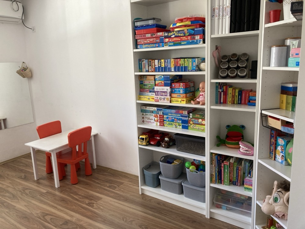 Rafturile cu jocuri, cărți și materiale de lucru, lângă măsuța copiilor